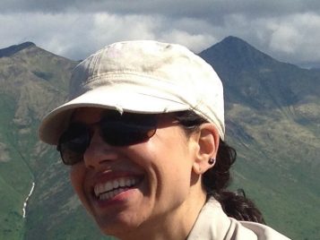 Raven Garvey smiling, wearing a tan cap, with mountains in the background.